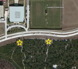 Aerial view of a landscape showing a sports center, roads, and wooded areas with two yellow stars marking specific locations.